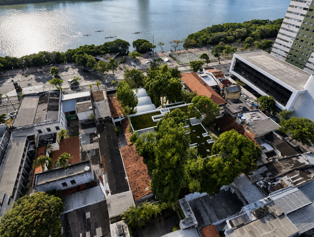 Vista aérea da área próxima ao rio, mostrando a implantação do centro entre construções existentes e árvores de grande porte, com cobertura verde integrada à vegetação.